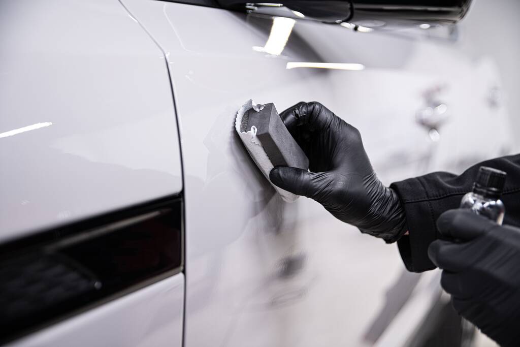 Employee of a car detailing studio applies a ceramic coating to a white car